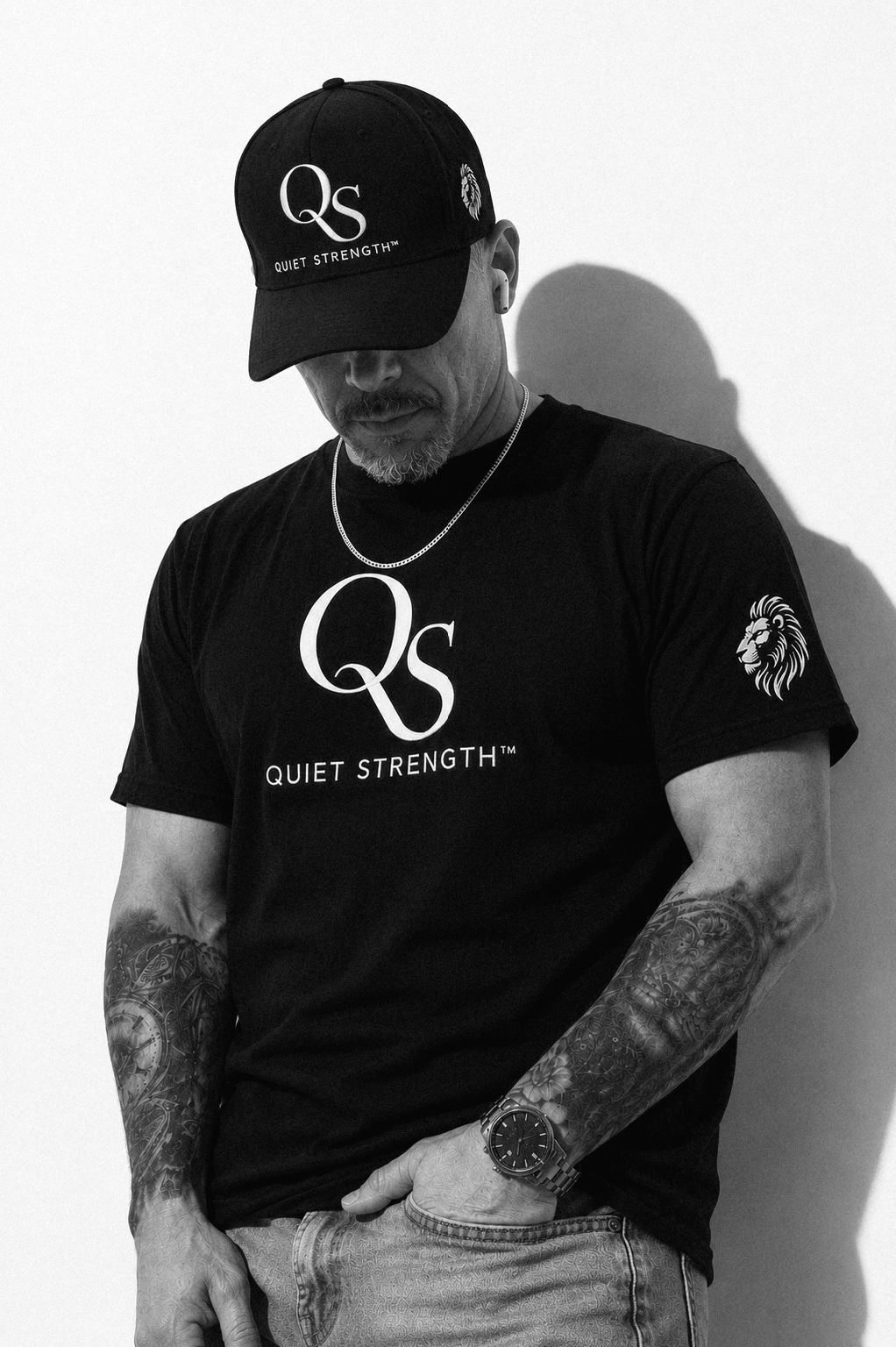 Man wearing a black QS Quiet Strength tee and QS snapback against a dark background